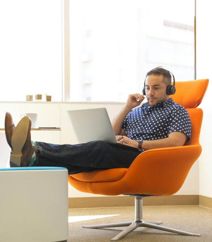 A man relaxes while working remotely in a modern office with a laptop and headphones.