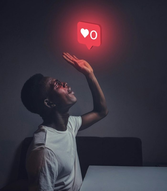 A man sits indoors reaching towards a glowing social media notification icon.